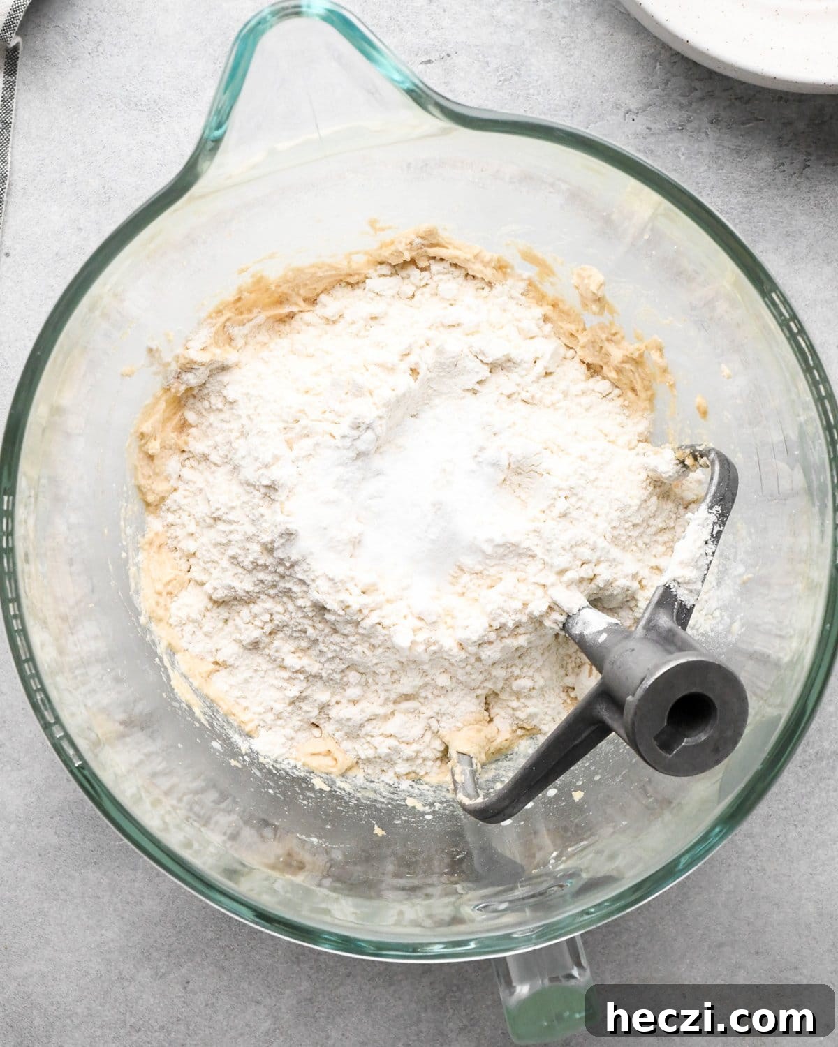 making cookie dough brownies - dry ingredient mixture added to the wet ingredient mixture in a glass mixing bowl with the paddle attachment int he bowl before mixing