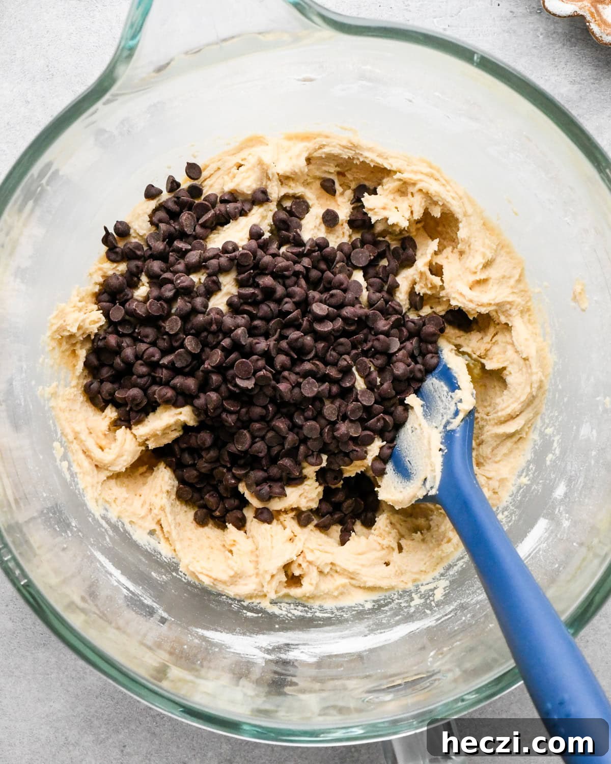 making cookie dough brownies - chocolate chips added to the cookie dough in a glass mixing bowl with a blue spatula.