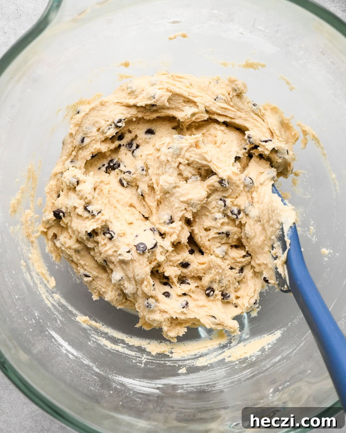 edible cookie dough in a glass bowl with a blue spatula to be used as the cookie dough layer in cookie dough brownies