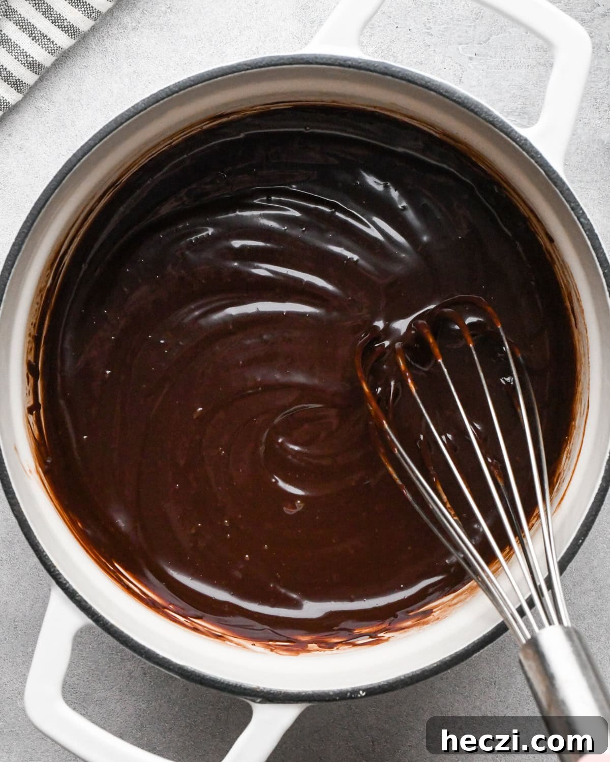 chocolate ganache for cookie dough brownies in a white pot with a whisk stirring the ganache