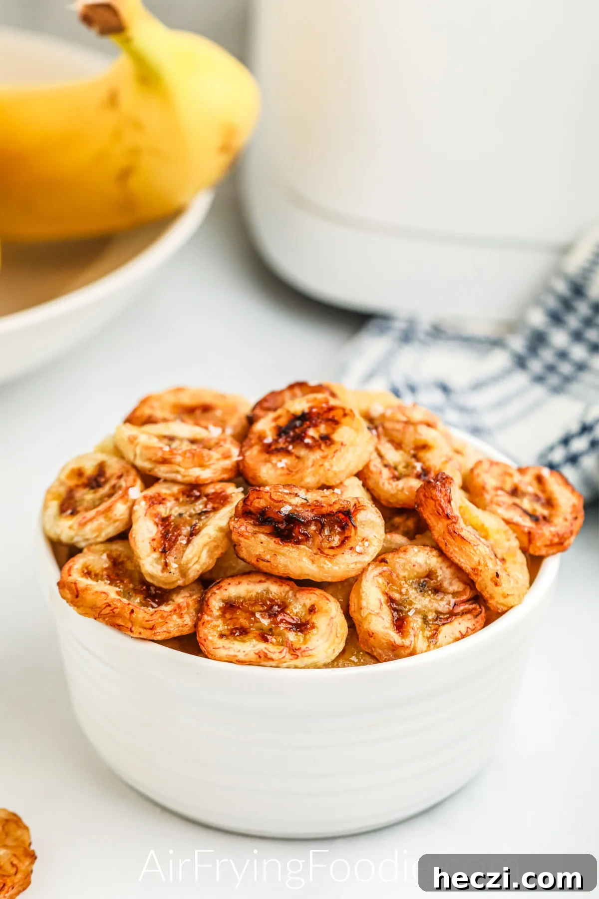 Crispy Air Fryer Banana Chips Recipe — Quick Snack at Home 3 Banana chips that were made in the air fryer, served in a white bowl and topped with kosher salt.