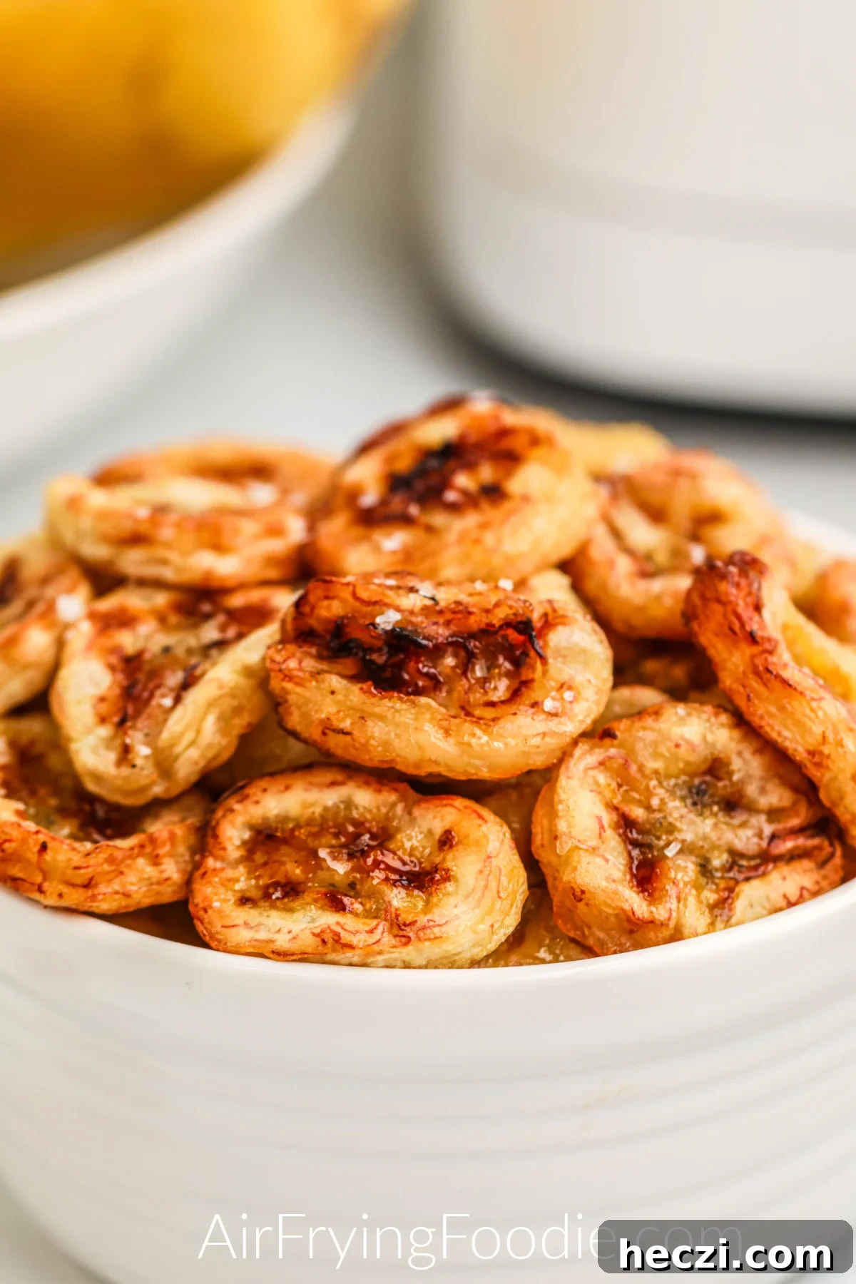 Crispy Air Fryer Banana Chips Recipe — Quick Snack at Home 9 Close up shot of banana chips made in the air fryer, and then placed in a white bowl and topped with kosher salt before serving.