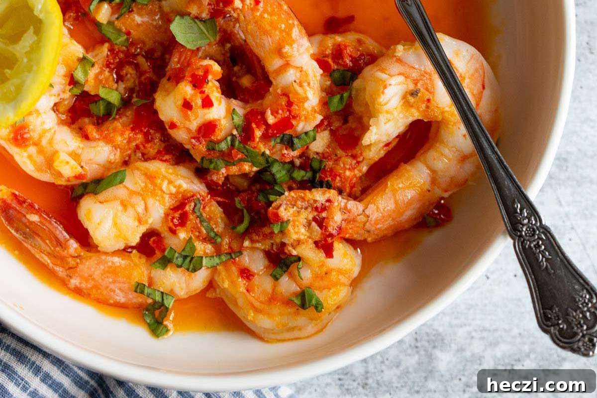 An Italian-inspired appetizer featuring a bowl of shrimp in a spicy sauce, served with lemon wedges.