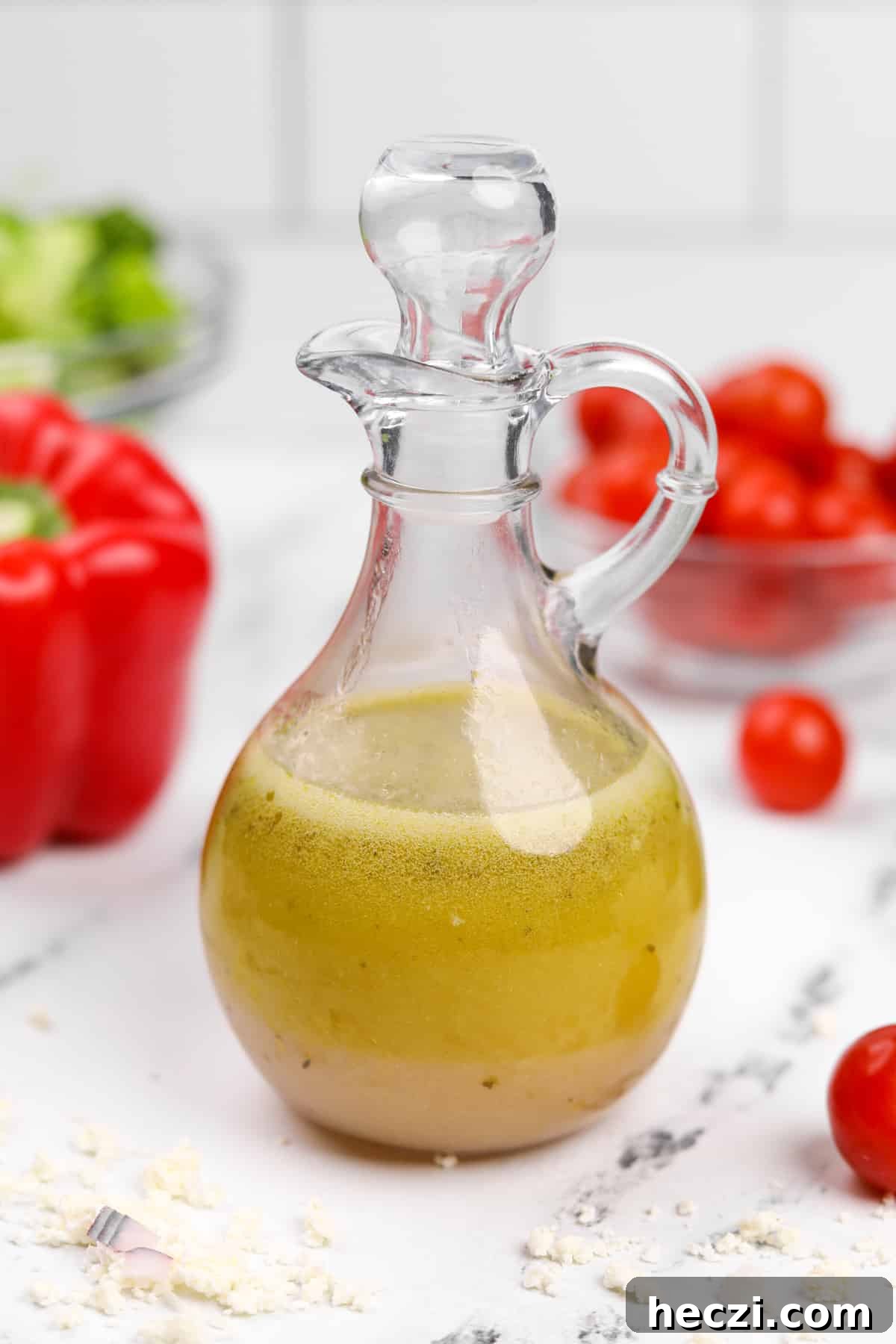 Authentic Greek Vinaigrette Recipe for Salads and Marinades 2 A cruet filled with homemade salad dressing, surrounded by red pepper, tomatoes, etc.