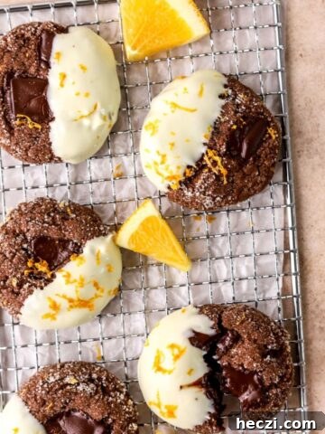 Chocolate cookies dipped in white chocolate on a wire rack with orange slices.