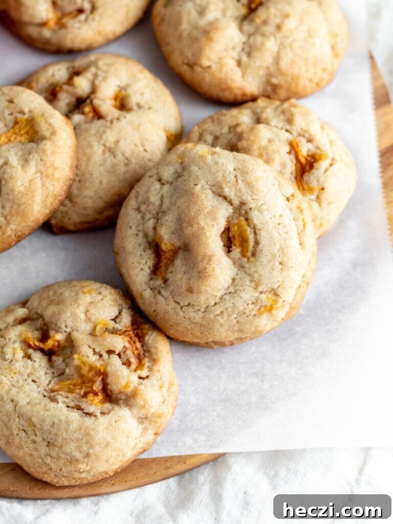 Peach Cobbler Cookies Recipe: Soft Peach Jam-Filled Cookies 8 Cookies with pieces of peaches baked inside on parchment paper.