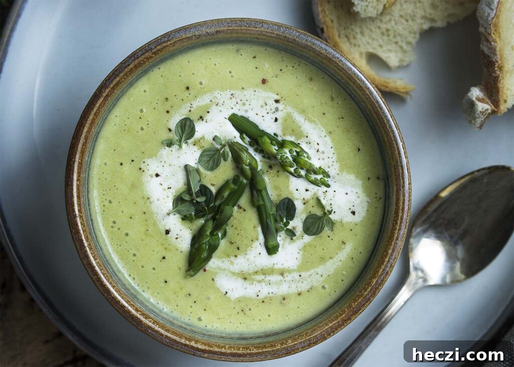 Close up top view of an earthenware bowl full of asparagus soup topped with cream, asparagus tips, and thyme.