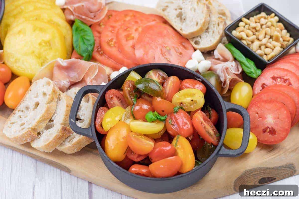 A charcuterie board with sliced tomatoes, bread, cherry tomatoes, prosciutto, mozzarella balls, basil, and a bowl of pine nuts.
