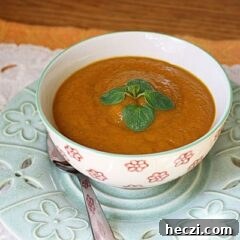 A close up photo of a bowl of pumpkin soup with a spoon on the side.