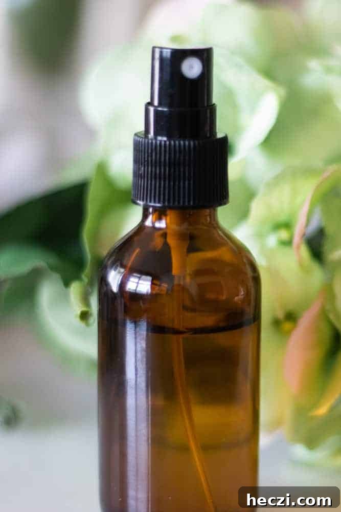 Mattress spray in amber glass spray bottle with green flowers behind it. 
