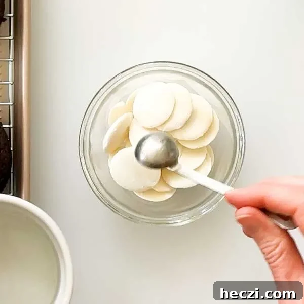 Adding coconut oil to white chocolate wafers in a glass bowl.