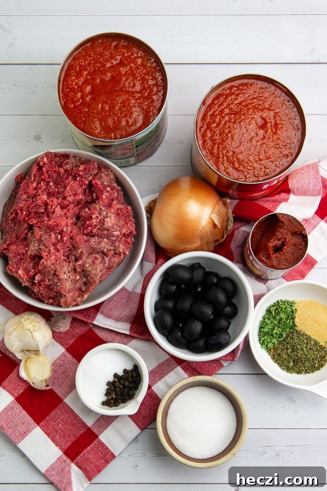 Authentic Homemade Spaghetti Sauce Recipe for Rich, Classic Flavor 3 A bowl of ground beef, an onion, a bowl of olives, a bowl of dried herbs, a bowl of salt, and several cans of tomato sauce on a white wooden table