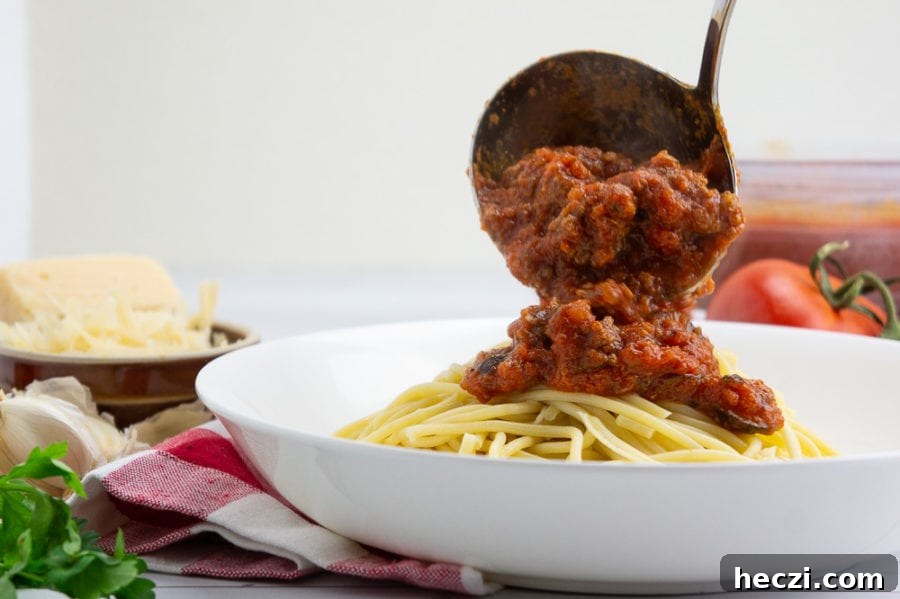 Authentic Homemade Spaghetti Sauce Recipe for Rich, Classic Flavor 6 a metal ladle pouring spaghetti sauce over a bowl of cooked spaghetti noodles.