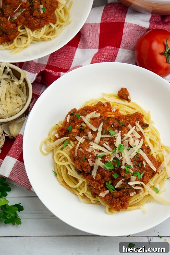 Authentic Homemade Spaghetti Sauce Recipe for Rich, Classic Flavor 7 a white bowl with spaghetti noodles and meat sauce with fresh parmesan and parsley on top, beside a red and white checked napkin