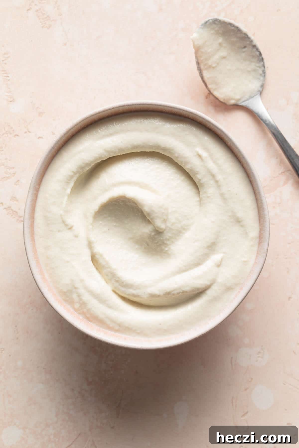 Creamy Cashew Vegan Mayo Recipe — Dairy-Free Mayonnaise 2 Overhead view of cashew mayo in a pink bowl with a spoon on the side.