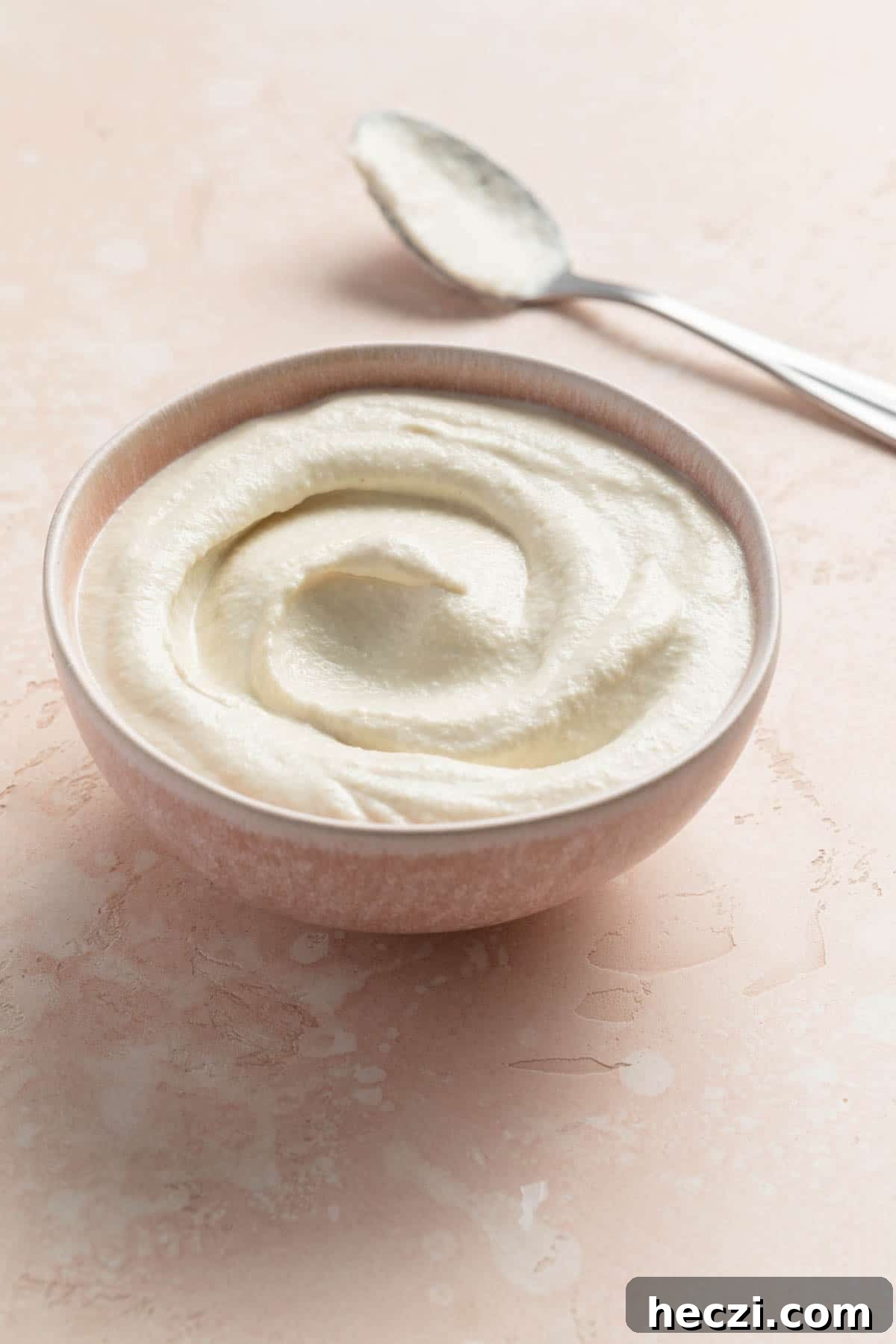 Creamy Cashew Vegan Mayo Recipe — Dairy-Free Mayonnaise 6 Three-quarter view of vegan cashew mayo in a small pink bowl with a spoon next to it.