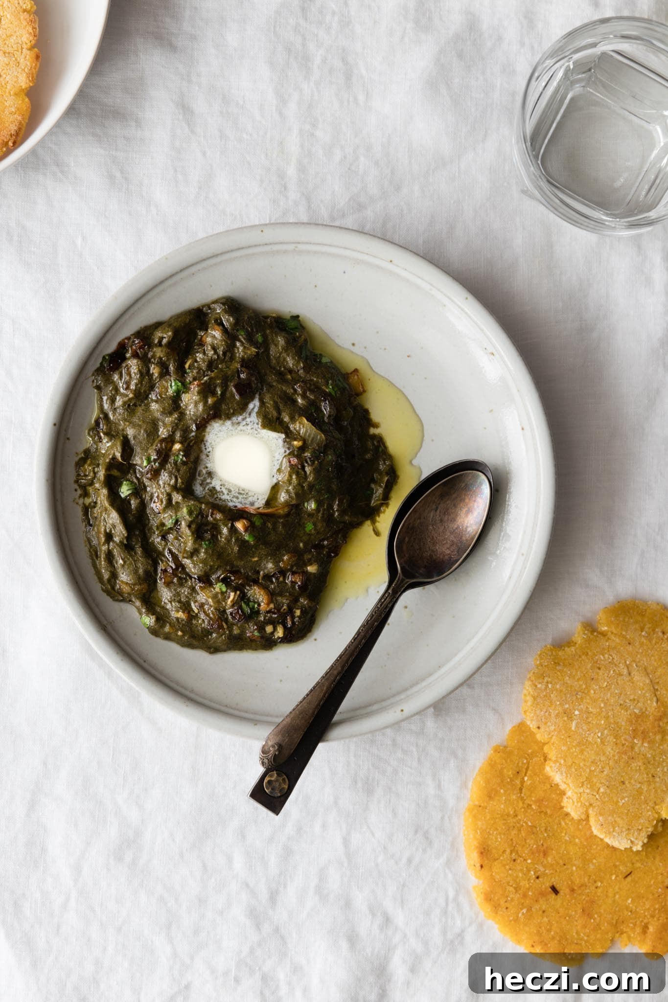 Sarson Ka Saag on a plate with a dollop of butter with makai ki roti on the side