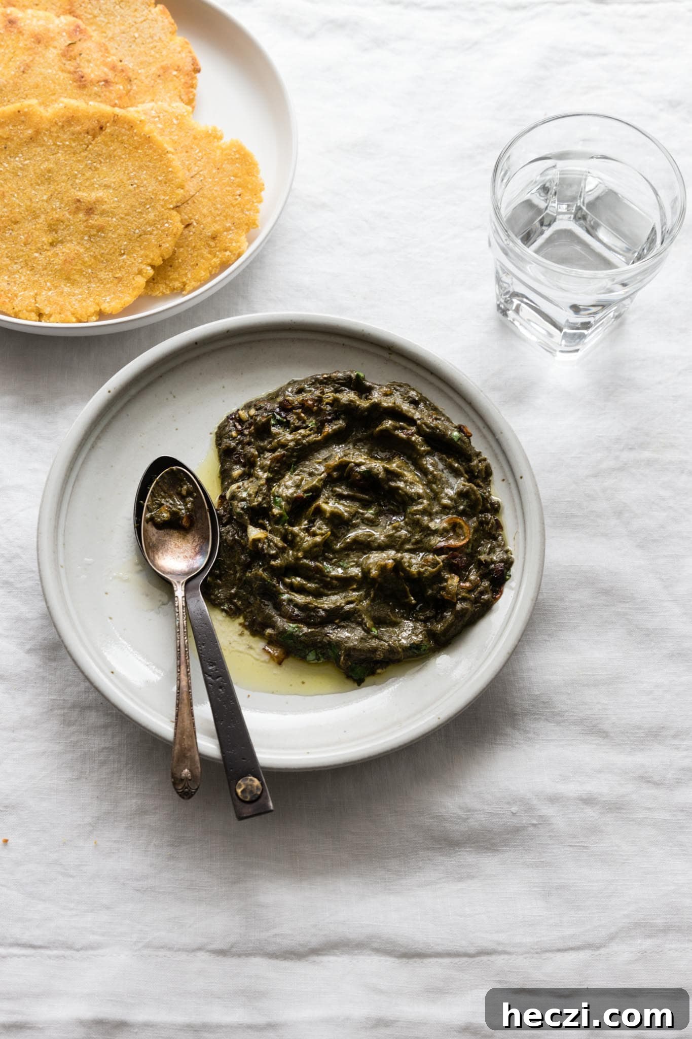 Easy Sarson Ka Saag on a plate with a couple spoons on the side served with makai ki roti (cornmeal flatbread) and a glass of water