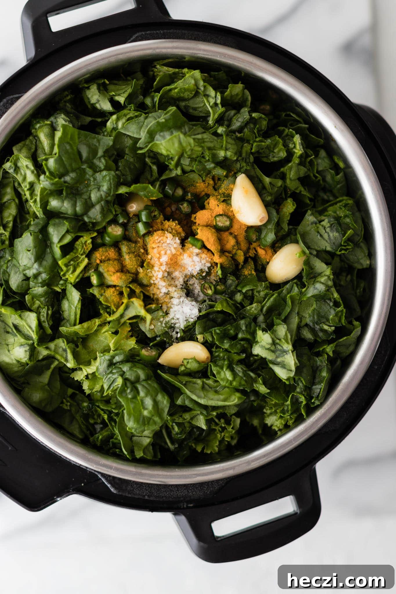 Instant Pot filled with mustard greens and spinach, garlic, green chili pepper and turmeric ready to be cooked to make Sarson Ka Saag