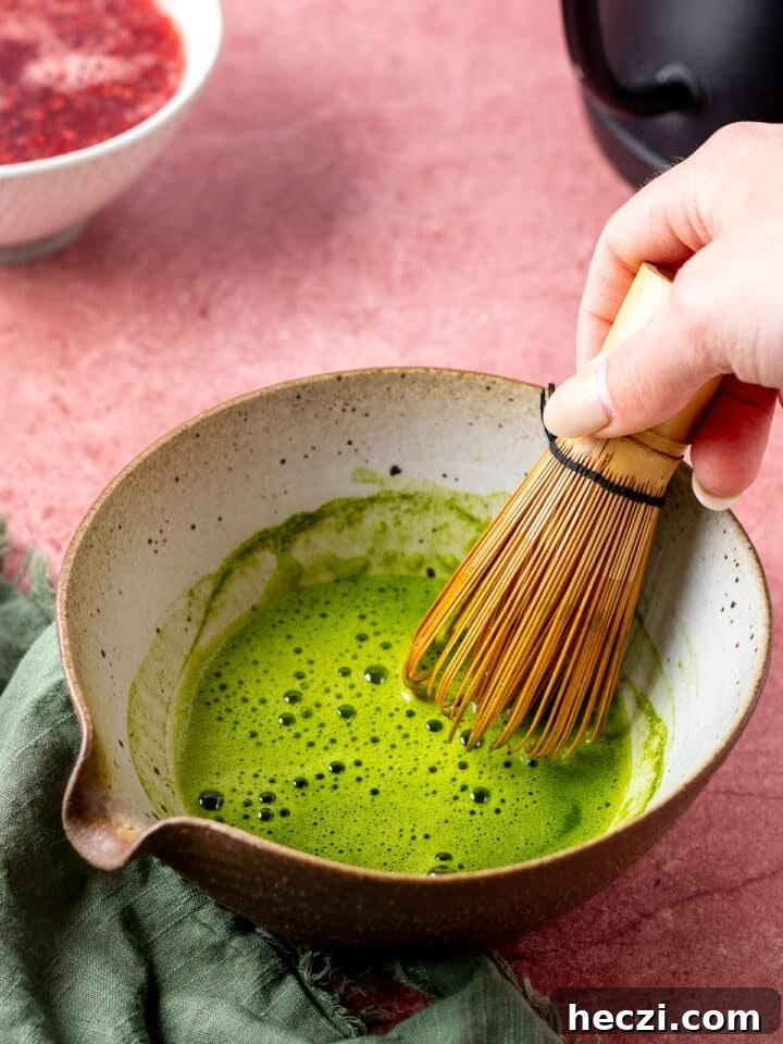 hand using a bamboo whisk to whisk matcha