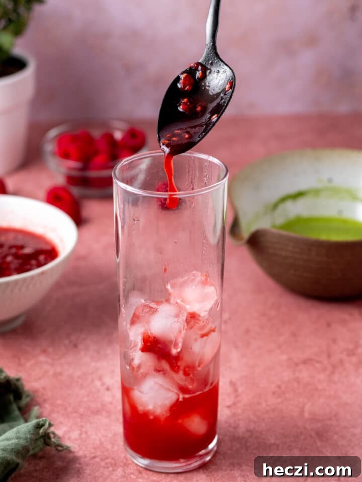 adding raspberry puree to a tall glass with ice