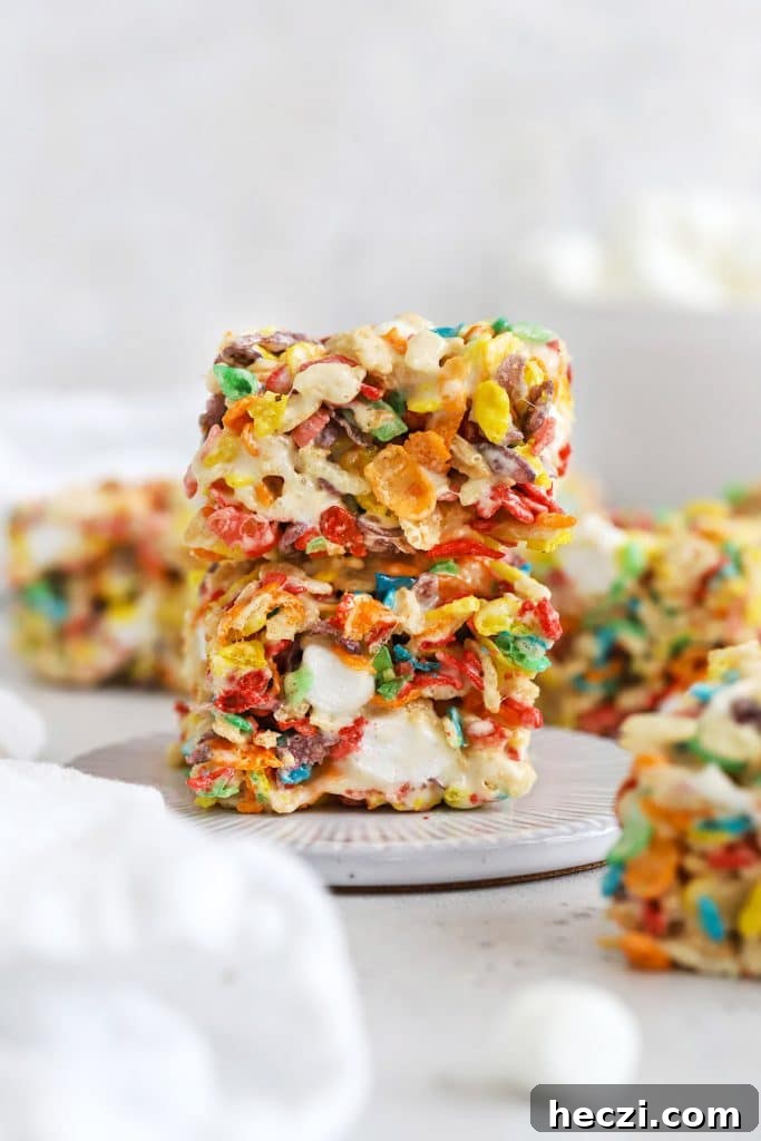 two fruity pebble rice krispies treats stacked on a white dessert plate