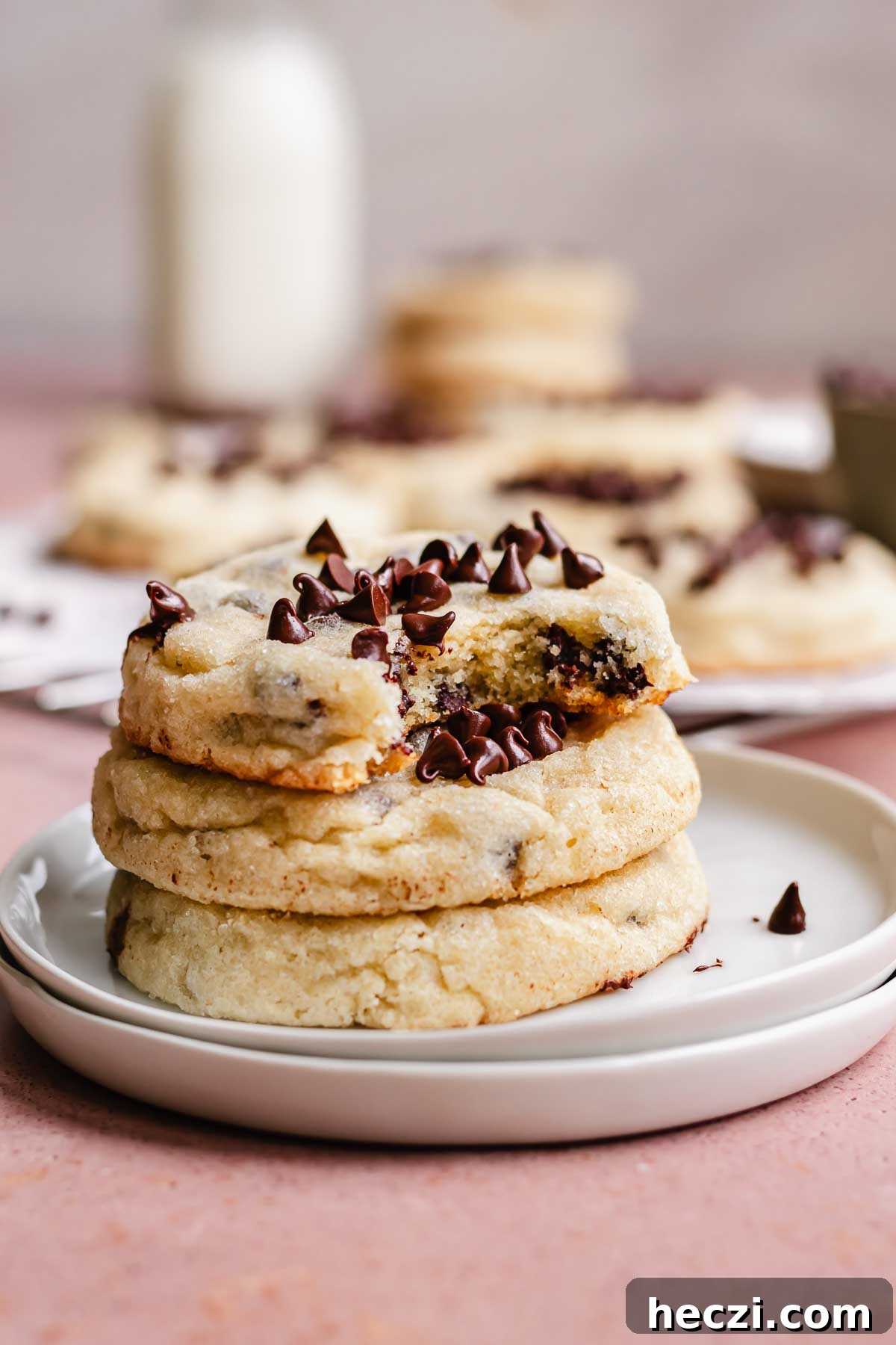 A stack of three chocolate chip sugar cookies on a plate. The top cookie has a bite removed.