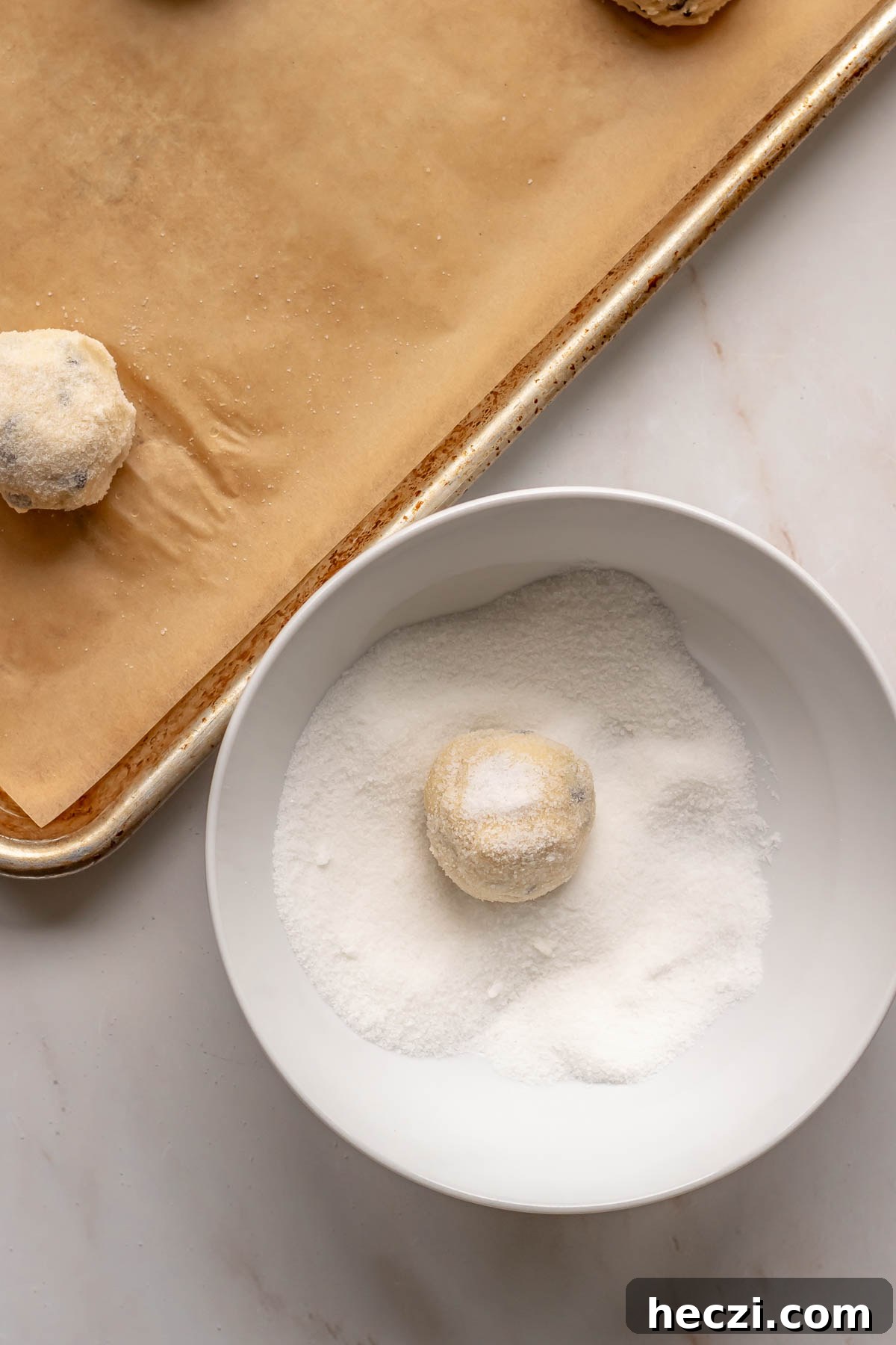 A ball of sugar cookie dough in a bowl of sugar.