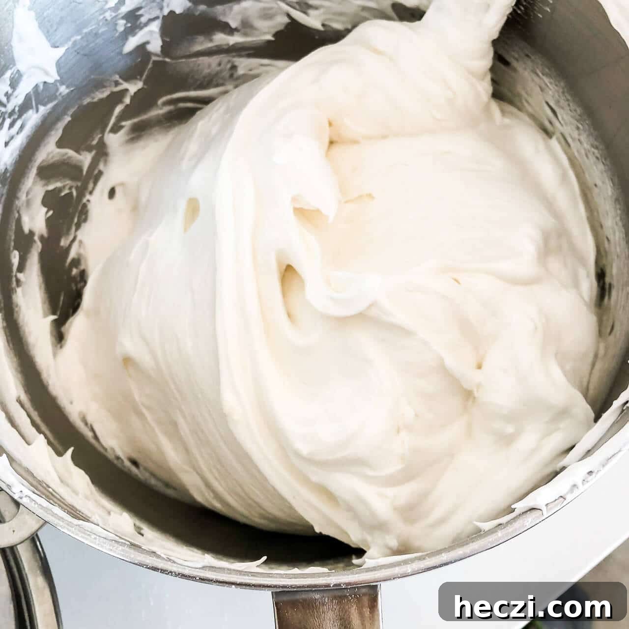 Photo demonstrating folding of whipped egg whites with flour to make angel food cake without deflating the mixture, in a big metal bowl using a large spatula