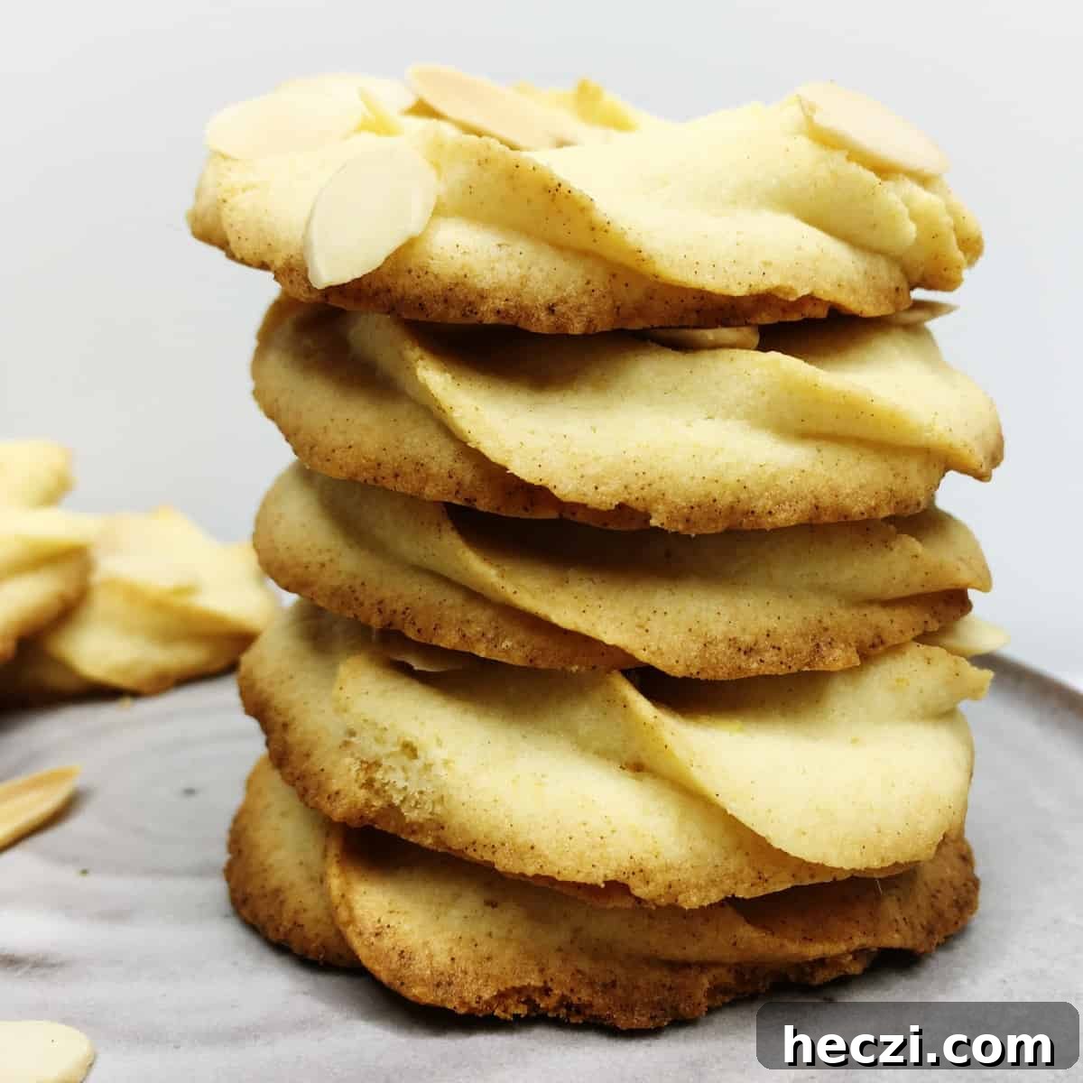Stacked Italian shortbread cookies on a grey plate with other cookies and almonds on background.