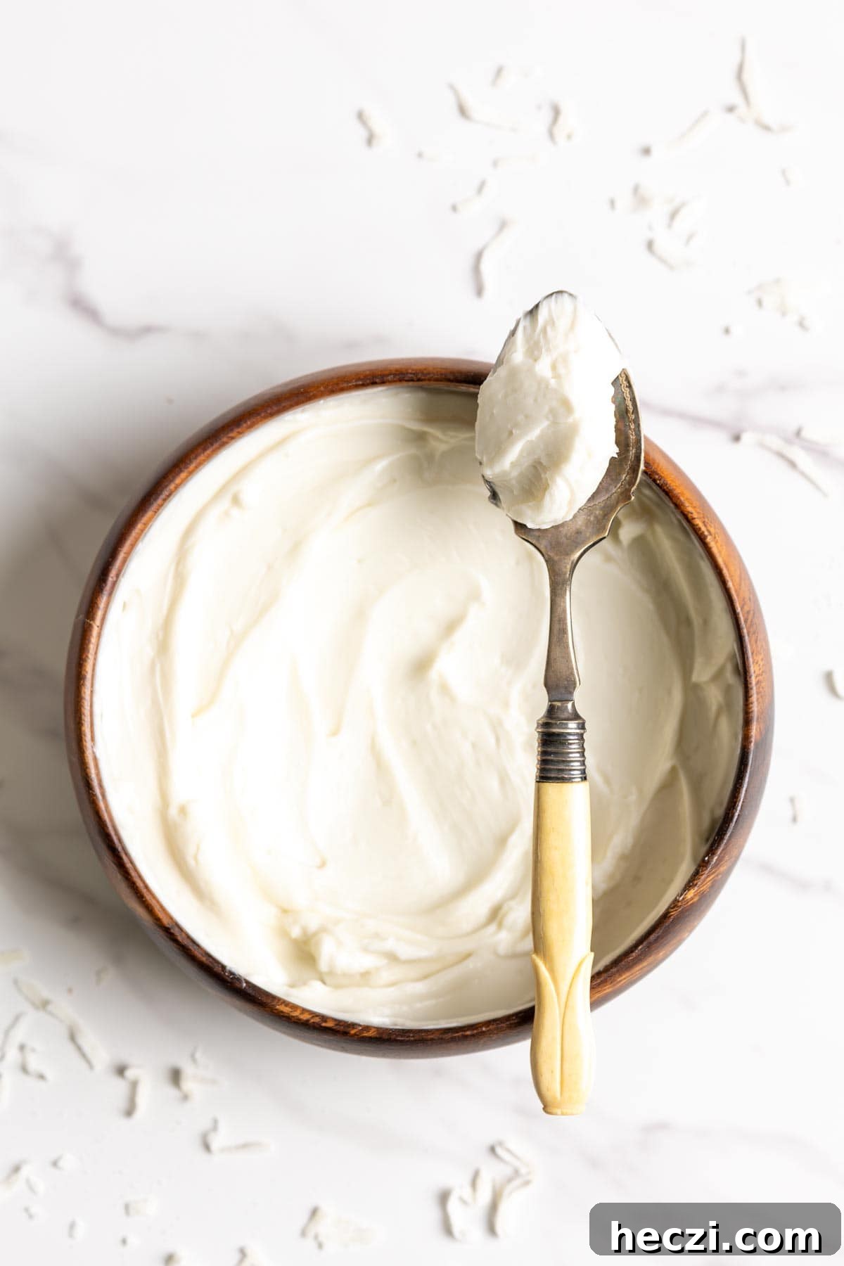 Coconut frosting in a wooden bowl with a spoon of frosting resting on top.