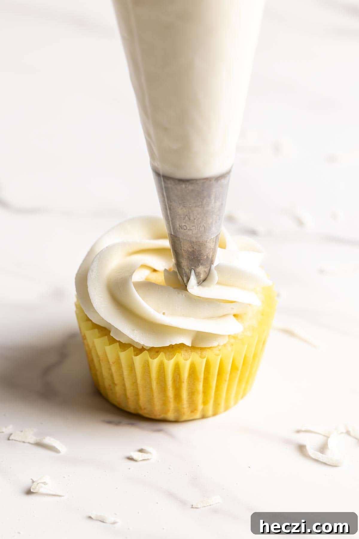 Coconut frosting is piped on a cupcake.