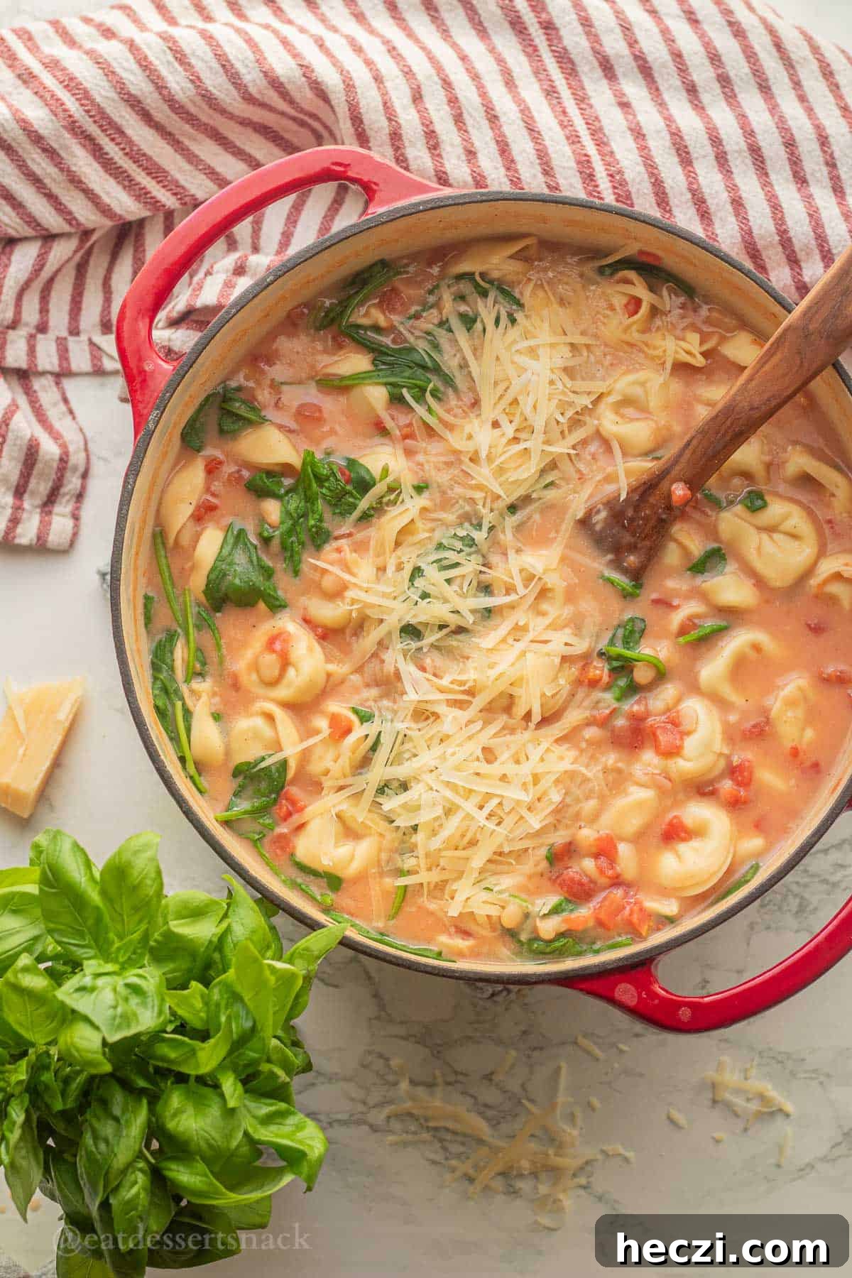 Tortellini tomato soup in pot with wooden spoon and basil.
