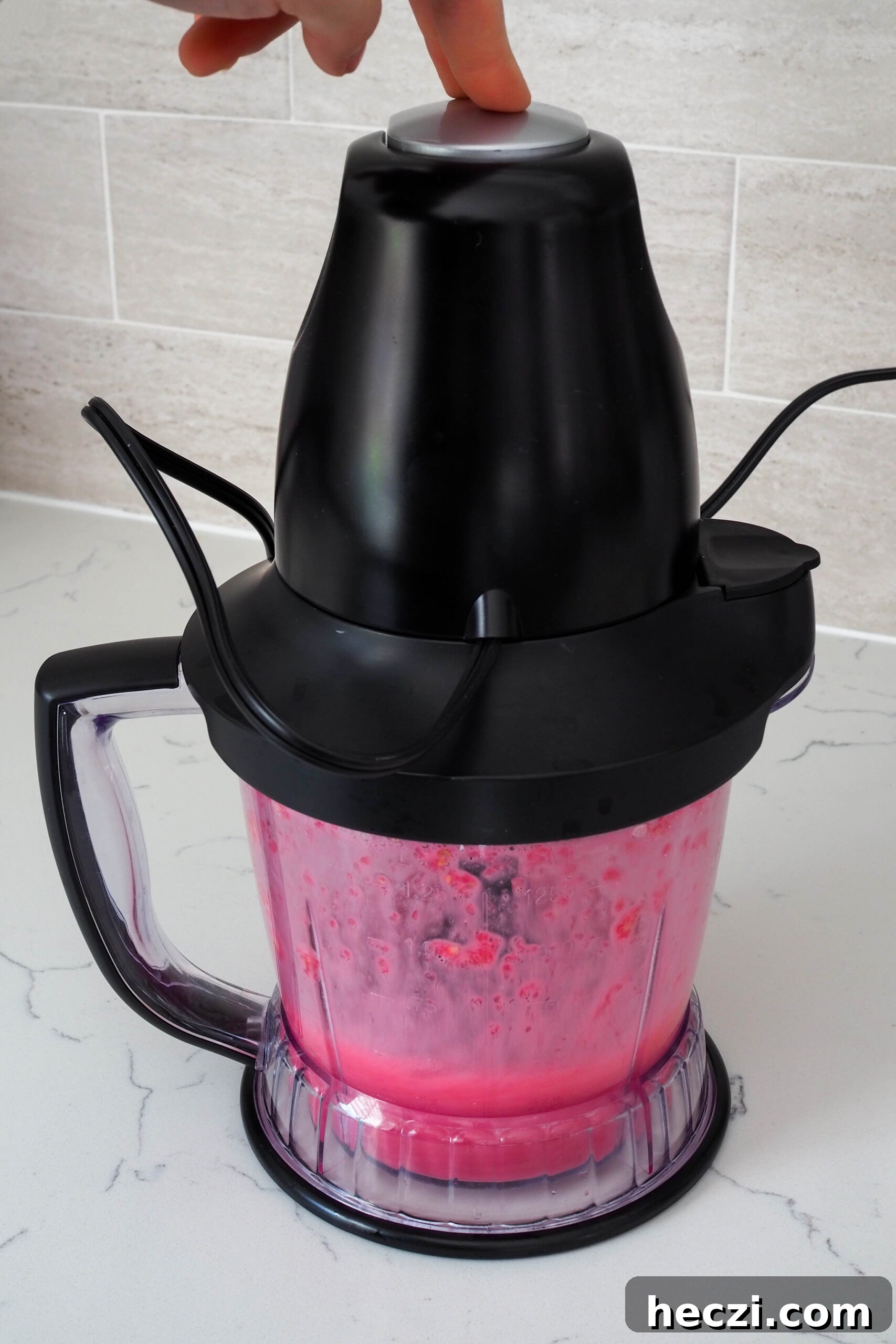 A hand presses down on a blender to blend dark red pomegranate juice.