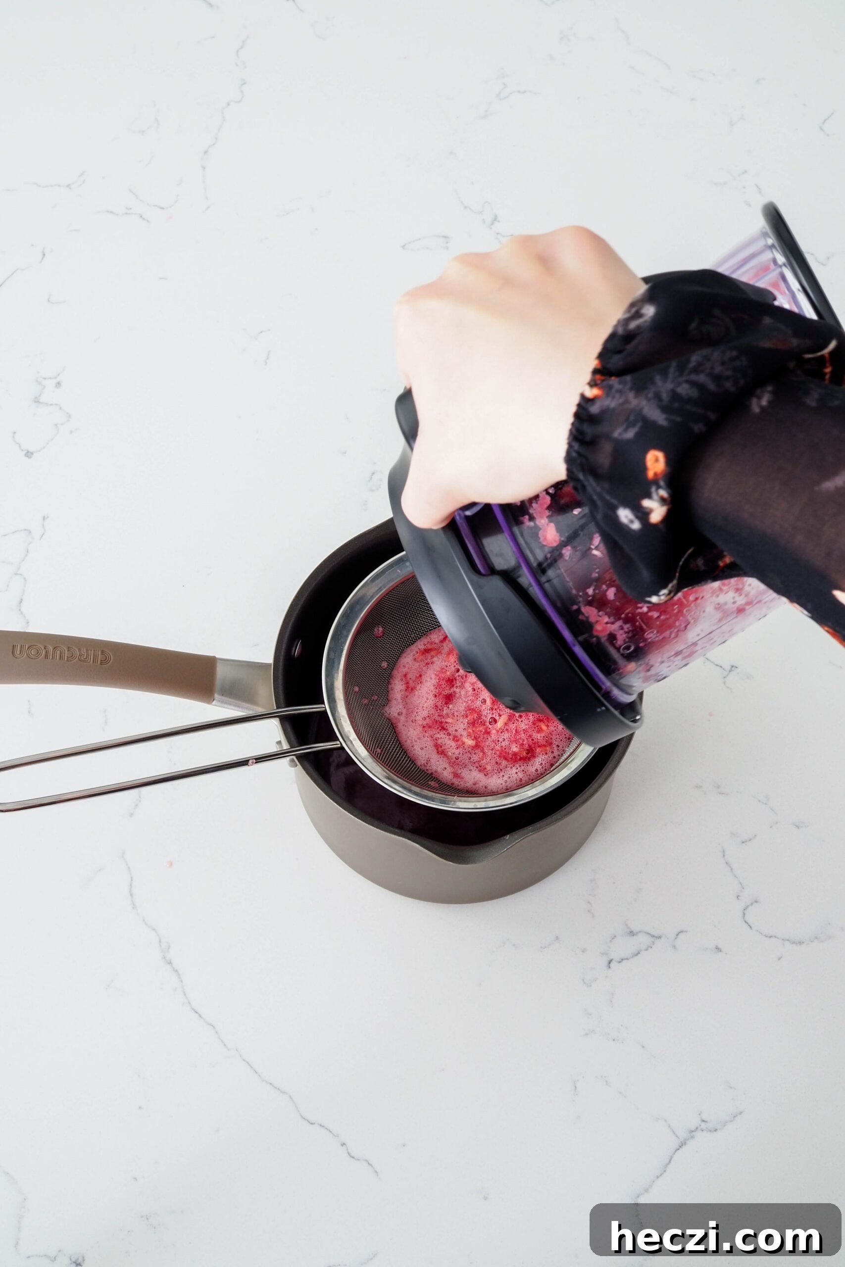 A hand pours pomegranate juice into a fine mesh strainer over a pot.