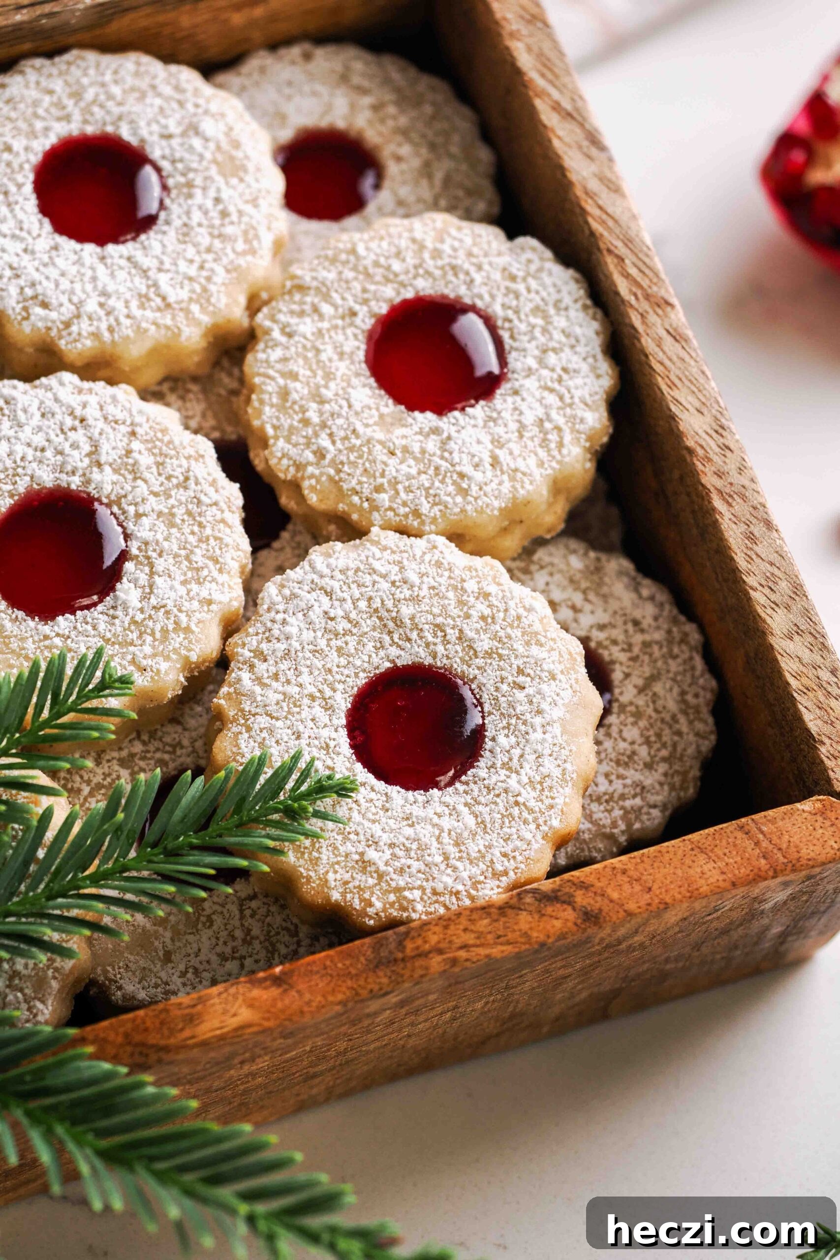 Linzer cookies filled with pomegranate jelly in a wooden box with pine branches.