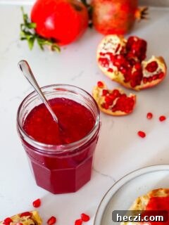A jar of pomegranate jelly with a spoon sticking out of it.