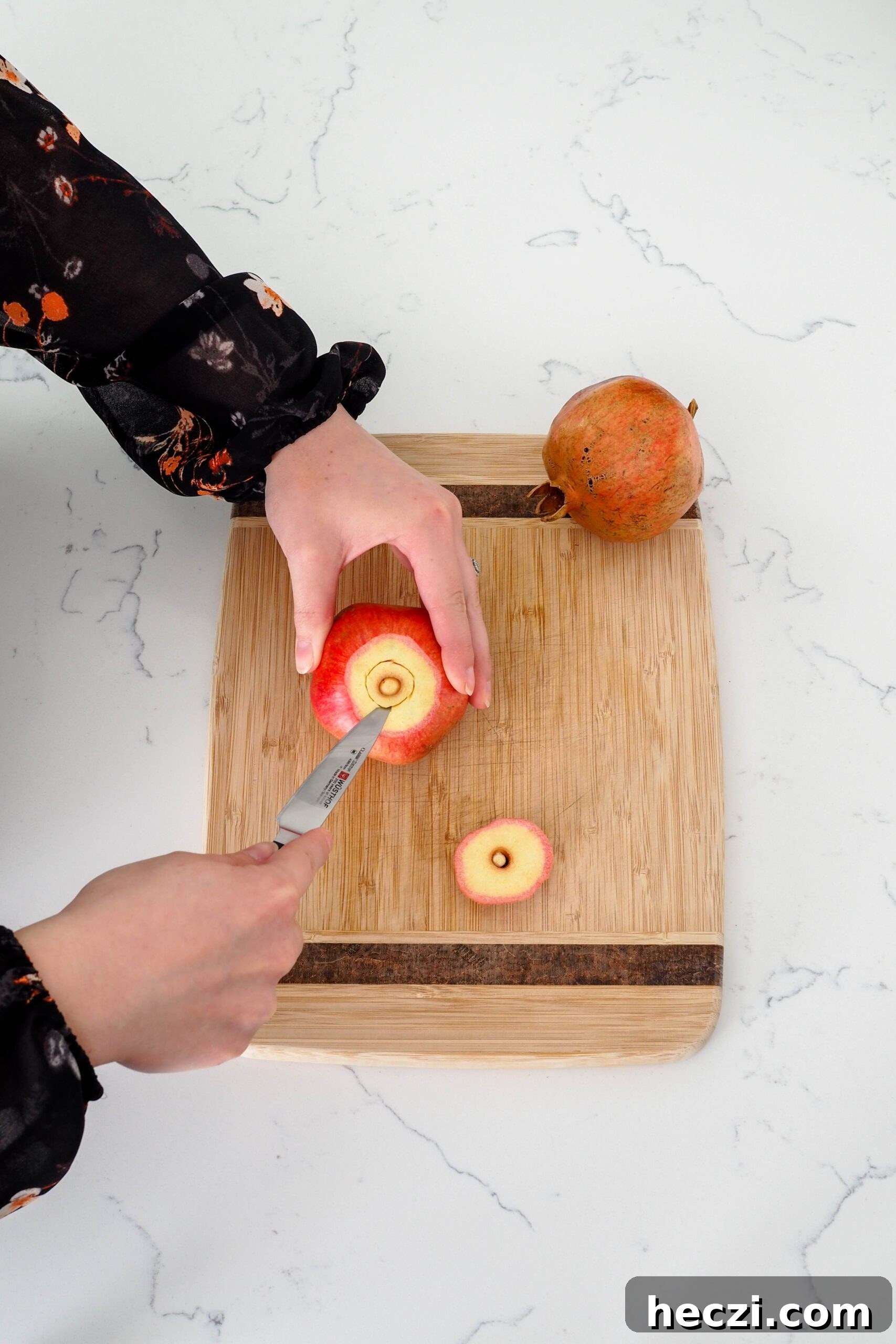 A paring knife cuts the thick membrane beneath the crown of the pomegranate out.