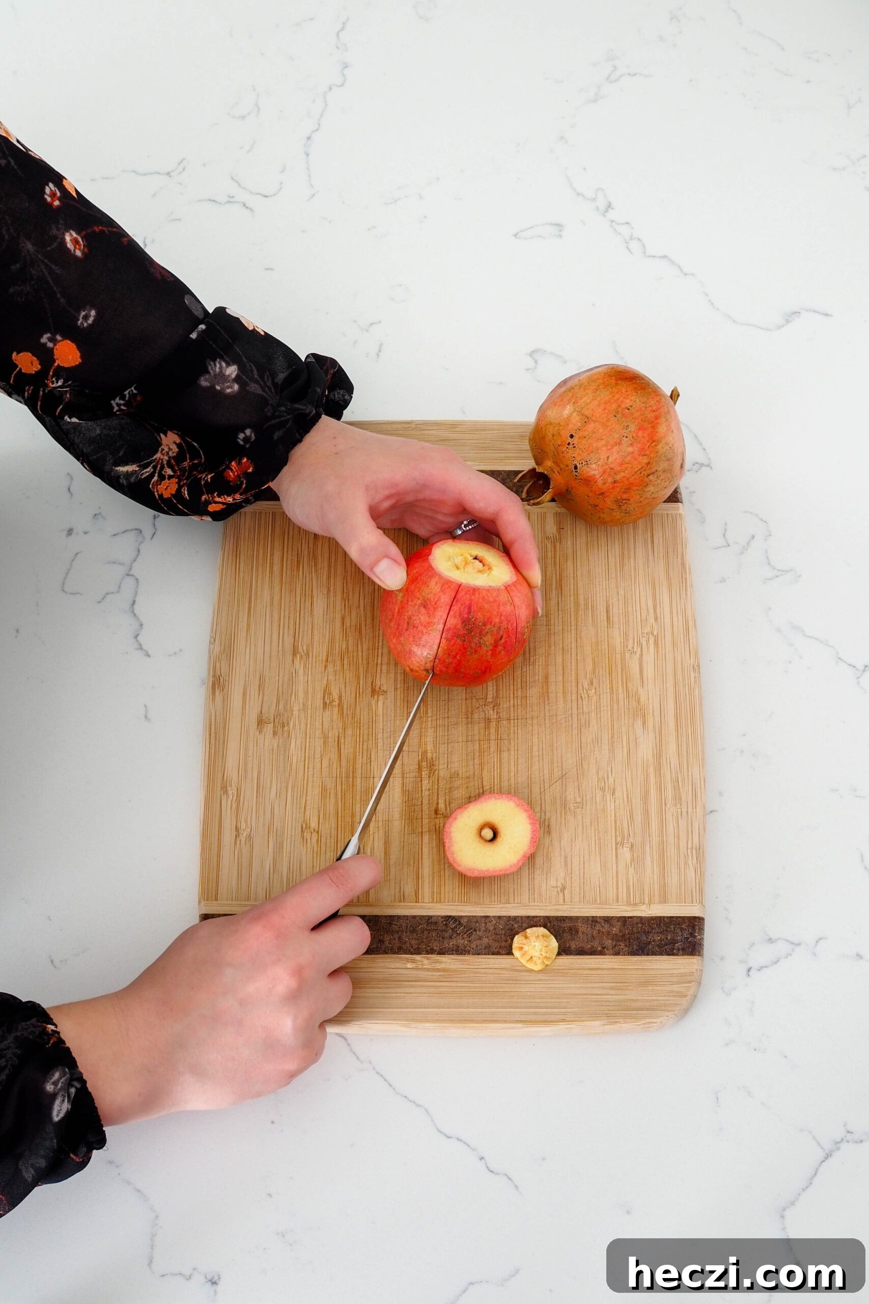A paring knife scores the edges of a pomegranate.