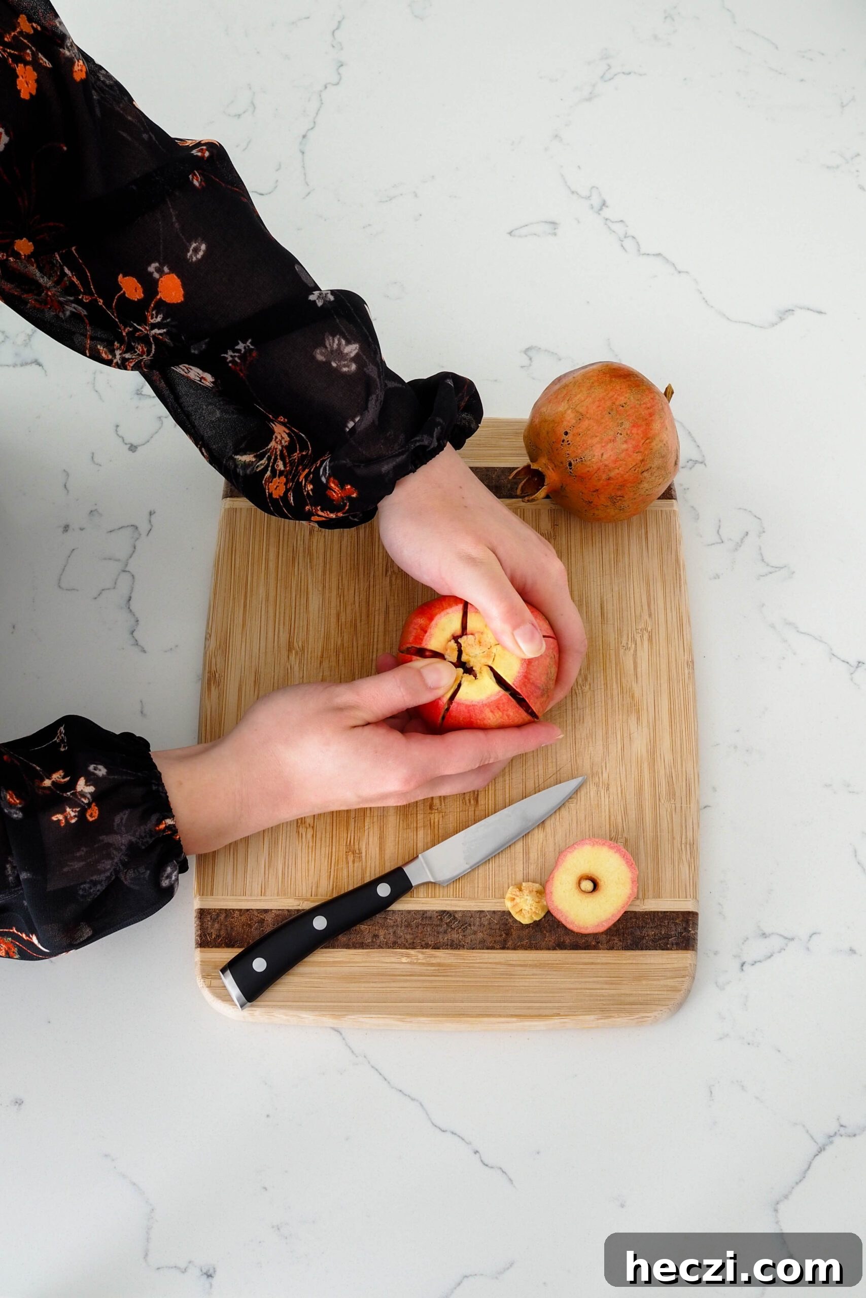 Two hands pull a cracked pomegranate apart.