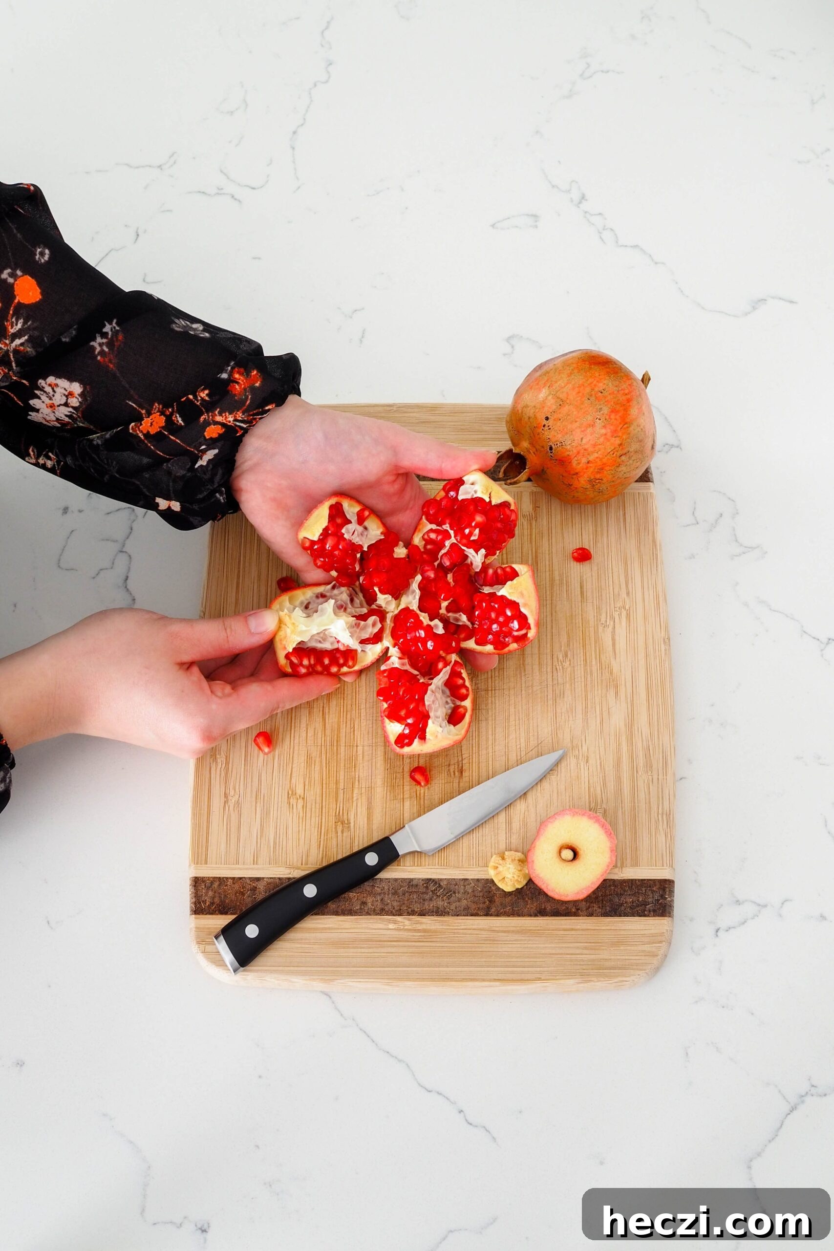 A hand pulls a section of pomegranate away from the fruit.