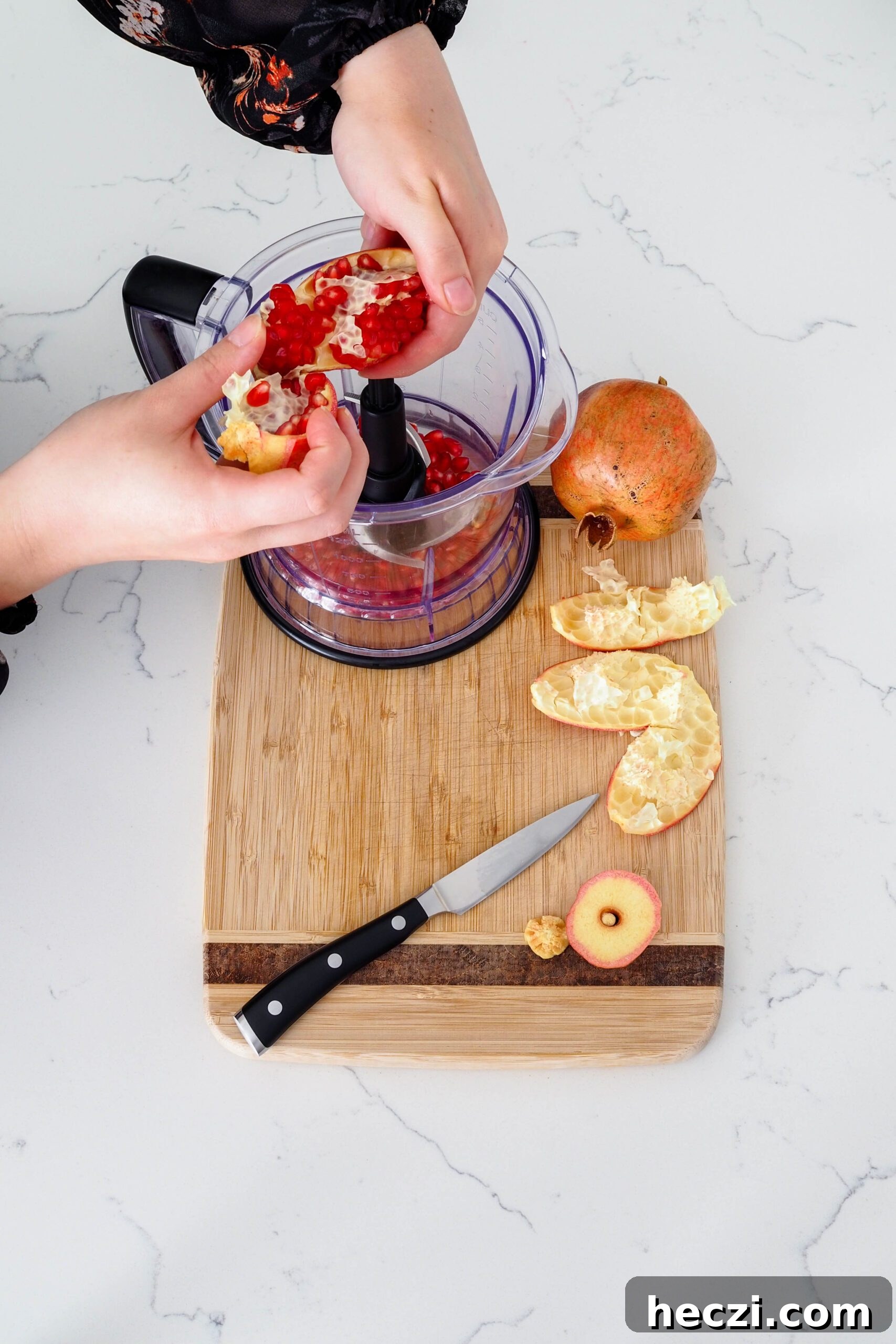 Two hands brush arils out of the pomegranate into the base of a blender.