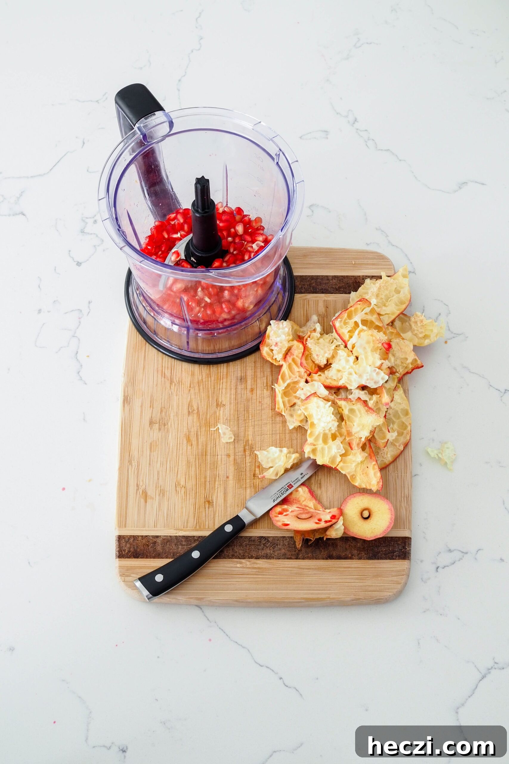 Pomegranate arils in the cup of a blender, with the pomegranate membrane leftovers on a cutting board.