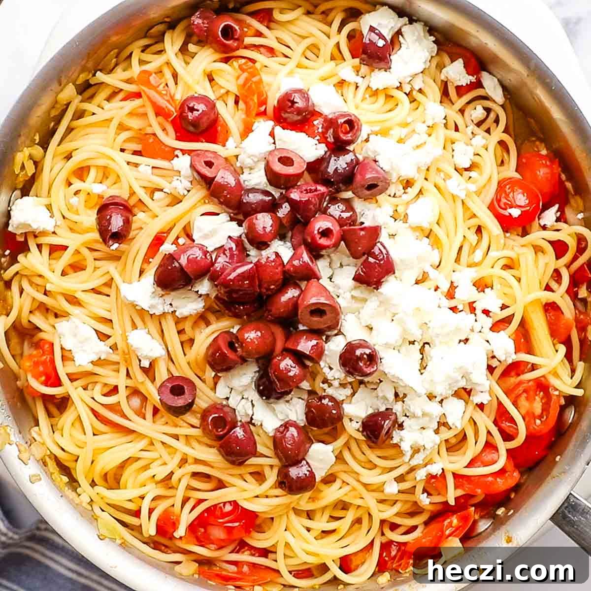 adding the kalamata olives and feta cheese to the greek spaghetti