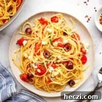 A plate of spaghetti with tomatoes, olives and feta.