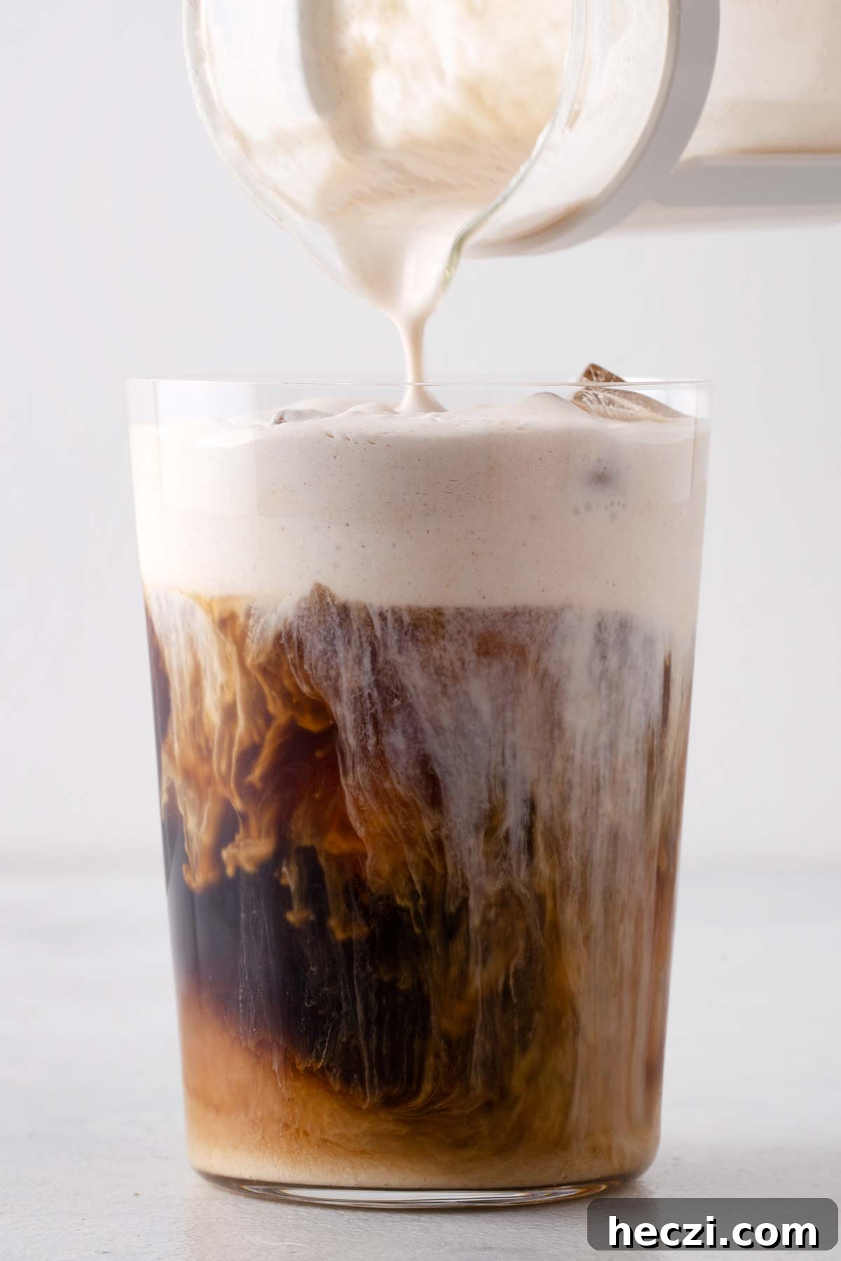 Brown Sugar Cold Foam being poured into a tall glass of iced coffee.