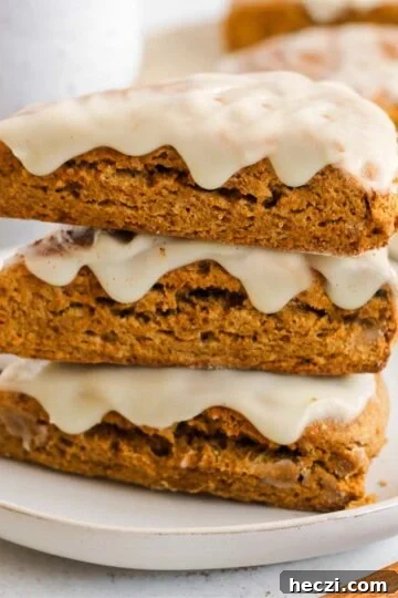 Pumpkin scones stacked 3 high on a plate with a ceramic mug and additional scones in the background.