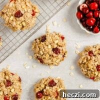 Multiple cranberry apple breakfast cookies spread out over a surface and cooling rack with a small dish of cranberries on the side.