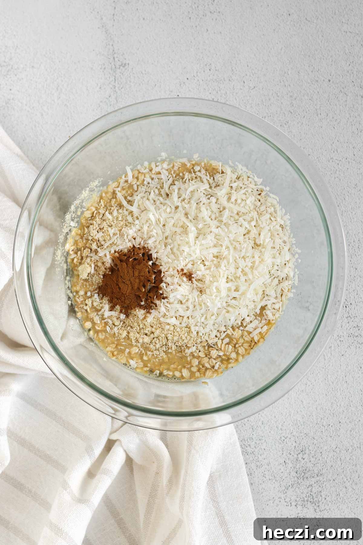 Whisked eggs and milk with oats, cinnamon, coconut and almond flour added to the top, all in a glass mixing bowl.