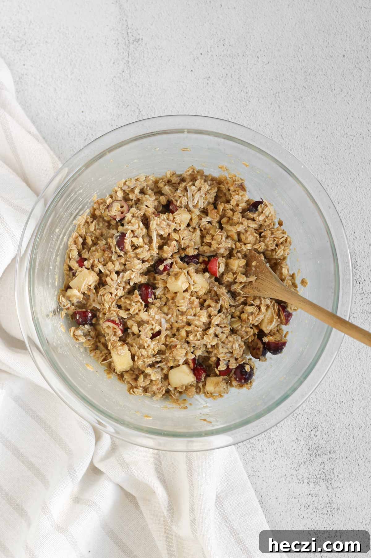 Cranberry apple breakfast cookie ingredients all mixed in a glass mixing bowl with a wooden spoon.